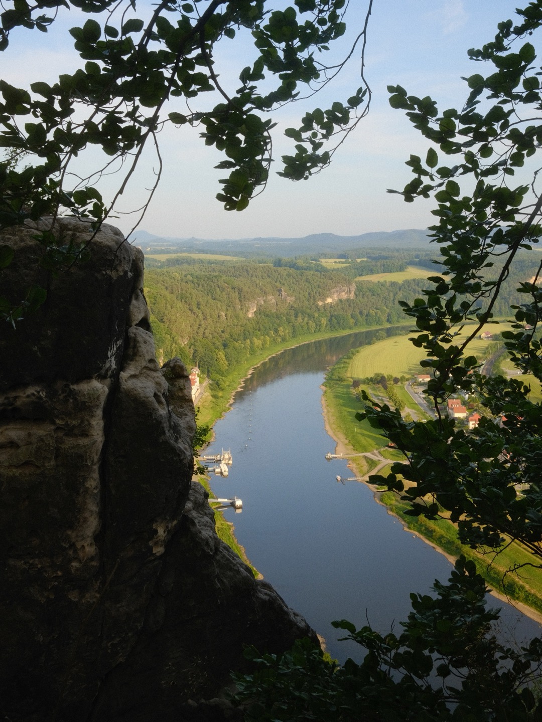 Blick zwischen Felsen und Ästen hinunter auf einen Fluss im Tal
